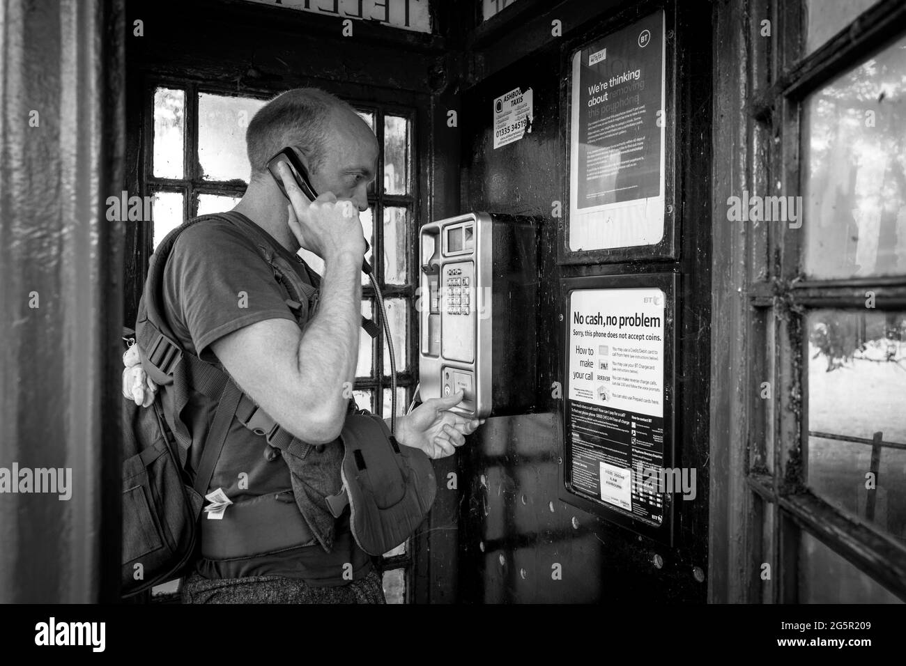 Ein Mann, der einen Anruf mit einem Hörer in einer britischen roten Telefonbox tätigen kann. Stockfoto