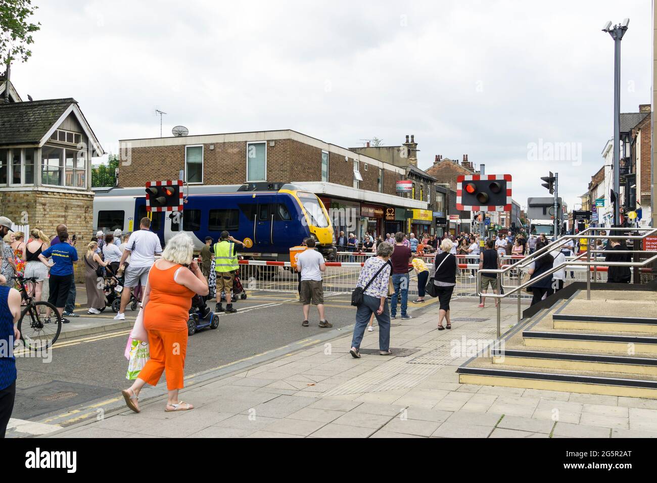 Fußgänger, die auf den Zug warten, um auf der High Street-Ebene über Lincoln City 2021 zu fahren Stockfoto