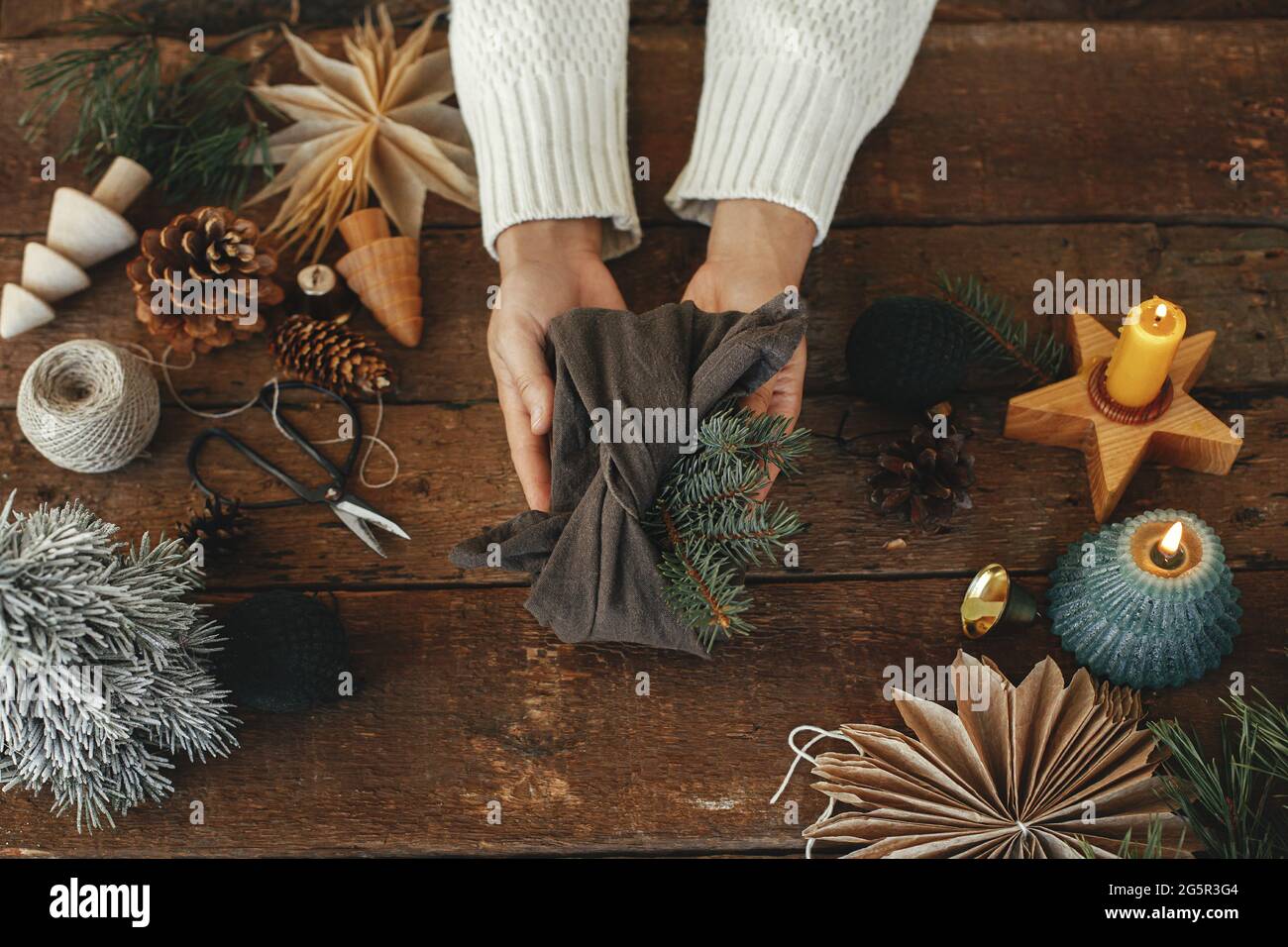Zero Waste Winterurlaub und Weihnachtsgeschenk Konzept. Hände halten stilvolle weihnachtsgeschenk Draufsicht auf rustikalen Holztisch mit Feiertagsdekorationen. Furos Stockfoto