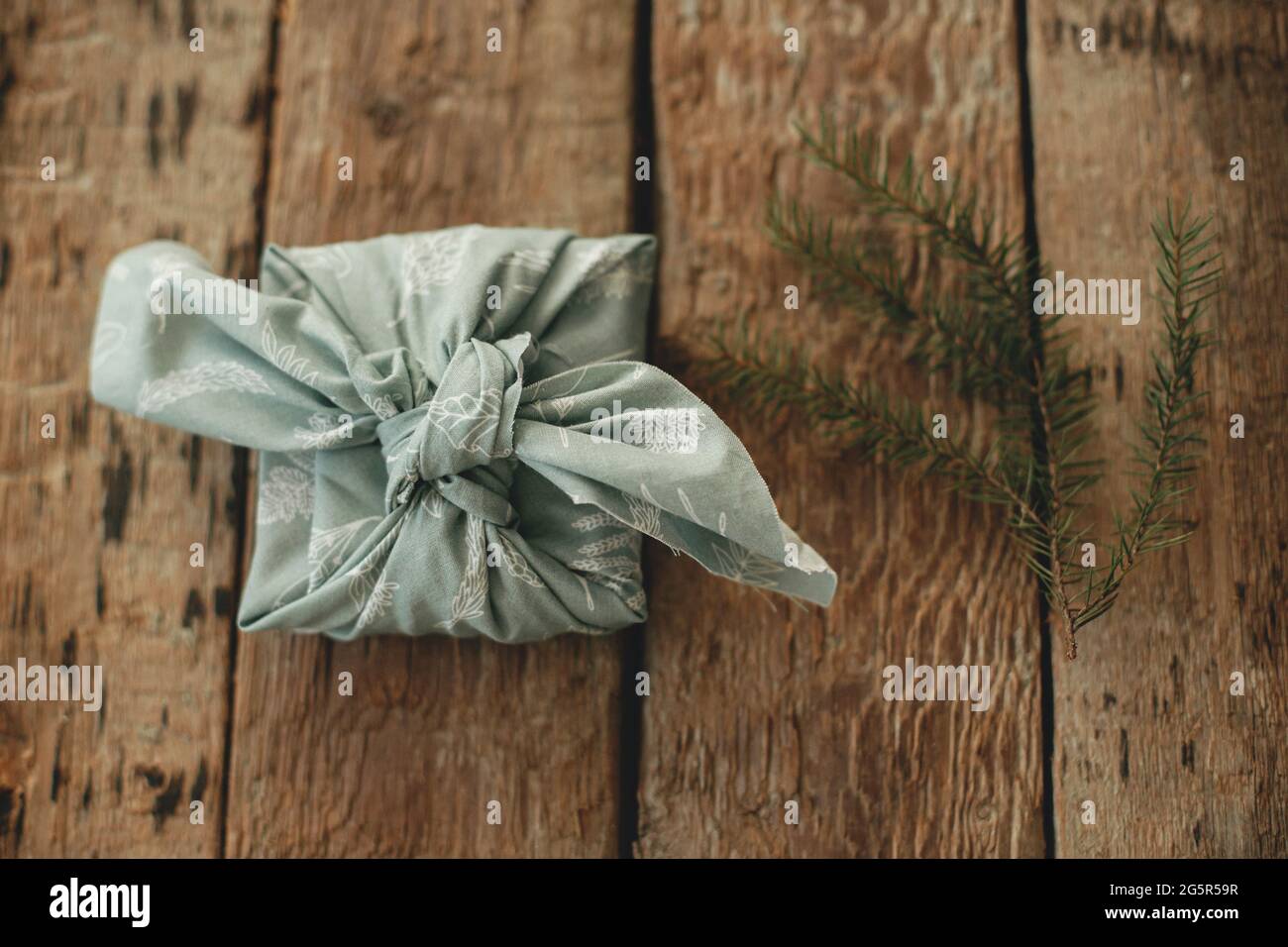 Null Verschwendung Winterferien und Geschenk. Furoshiki umweltfreundlich präsent. Stilvolles weihnachtsgeschenk in Stoff und Tannenzweig auf rustikalem Holztisch verpackt fl Stockfoto