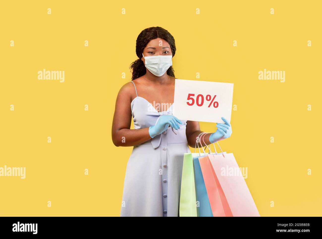 Schwarze Dame in medizinischen Maske und Gummihandschuhe mit Einkaufstaschen und FÜNFZIG PROZENT OFF-Zeichen, bietet riesigen Verkauf Stockfoto