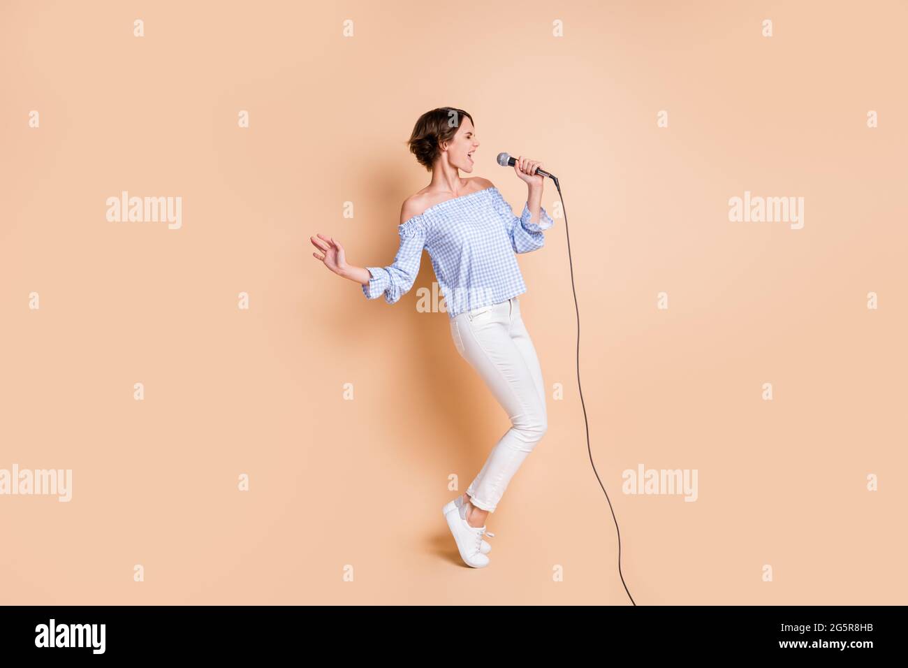 In voller Größe Profil Seite Foto von jungen aufgeregt Mädchen singen Mikrofon Konzert verrückt aussehen leeren Raum isoliert über beige Farbe Hintergrund Stockfoto