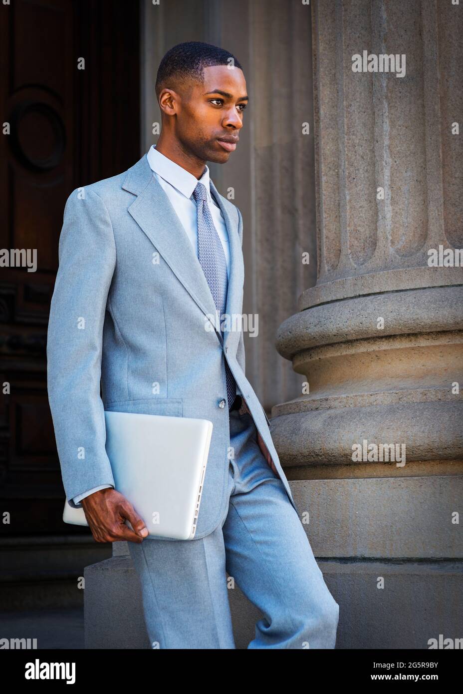 Ein junger afroamerikanischer Geschäftsmann, der einen hellgrauen Anzug,  eine weiße Unterhemd, eine Krawatte und einen Laptop trägt, geht vom Wintag  herunter Stockfotografie - Alamy