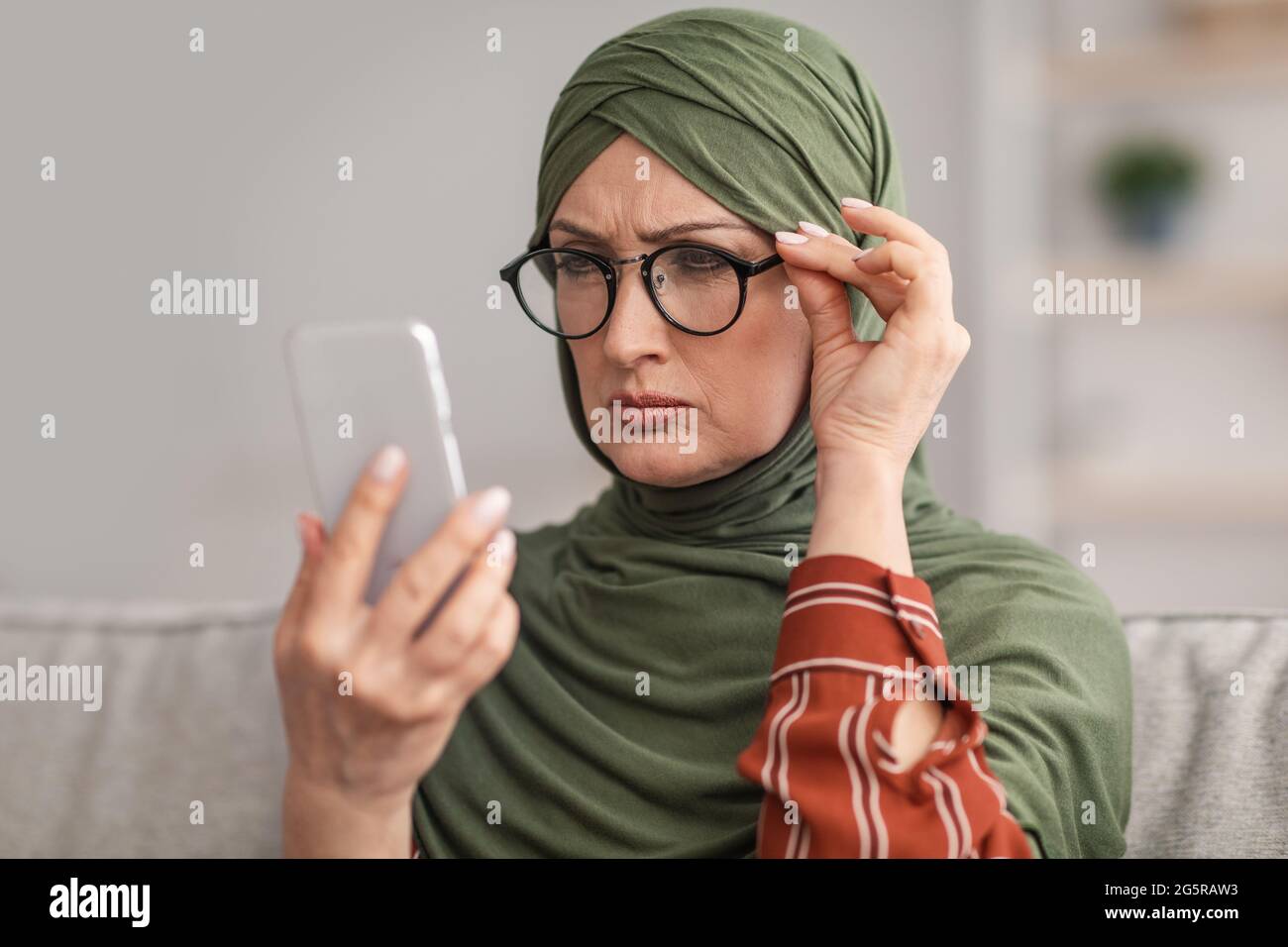 Ältere Frau Aus Dem Nahen Osten In Einer Brille, Die Augen Schielt, Liest Nachricht In Der Halle Stockfoto