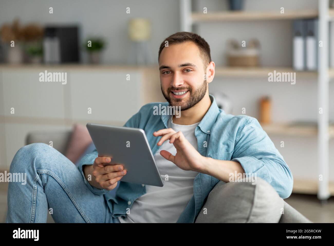Online-Life-Konzept. Glücklicher junger Mann, der Tablet-Computer benutzt, von zu Hause aus arbeitet oder studiert Stockfoto