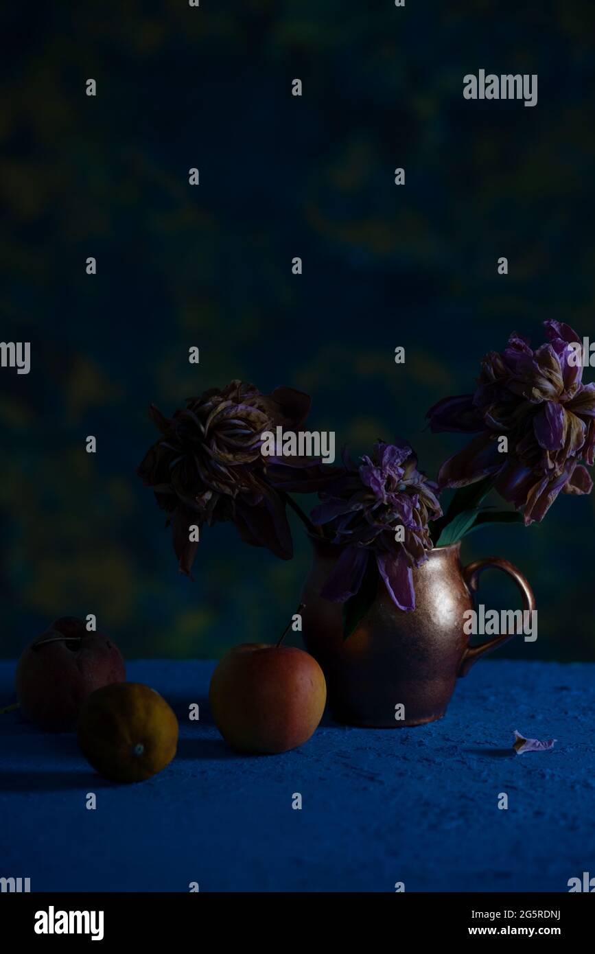 Dramatisches Stillleben im Vintage-Stil mit einem Bouquet aus welkenden Blumen in einer Kupfervase. Das Konzept des vergehenden Sommers. Stockfoto