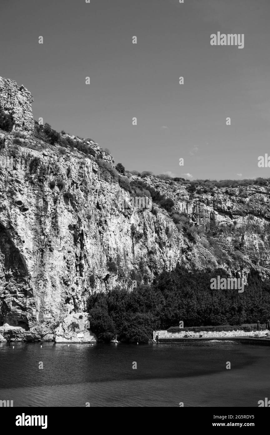 Vouliagmeni See in Griechenland an sonnigen Sommertagen. Kleiner Brackwassersee gespeist. Malerische Landschaft mit weißen Bergen und grünem Wasser. Thermalquelle. SPA Stockfoto