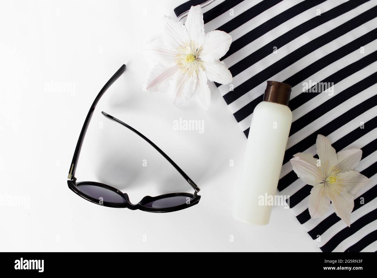 Sommer flach Lay. Sommersandalen, weiße Blumen, Sonnenbrillen und eine weiße Flasche.Draufsicht. Kreativer Hintergrund. Stockfoto