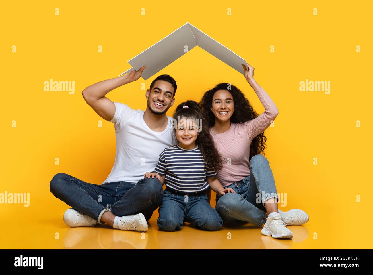 Familienhaus. Happy Arab Family Of Three Sitting Under Carton Roof Stockfoto