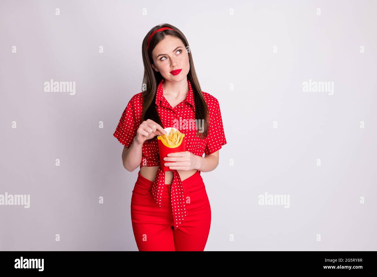 Foto von verträumt gesinnten Mädchen halten Papier-Box Fast Food suchen leeren Raum tragen rot gepunktete Bluse isoliert graue Farbe Hintergrund Stockfoto