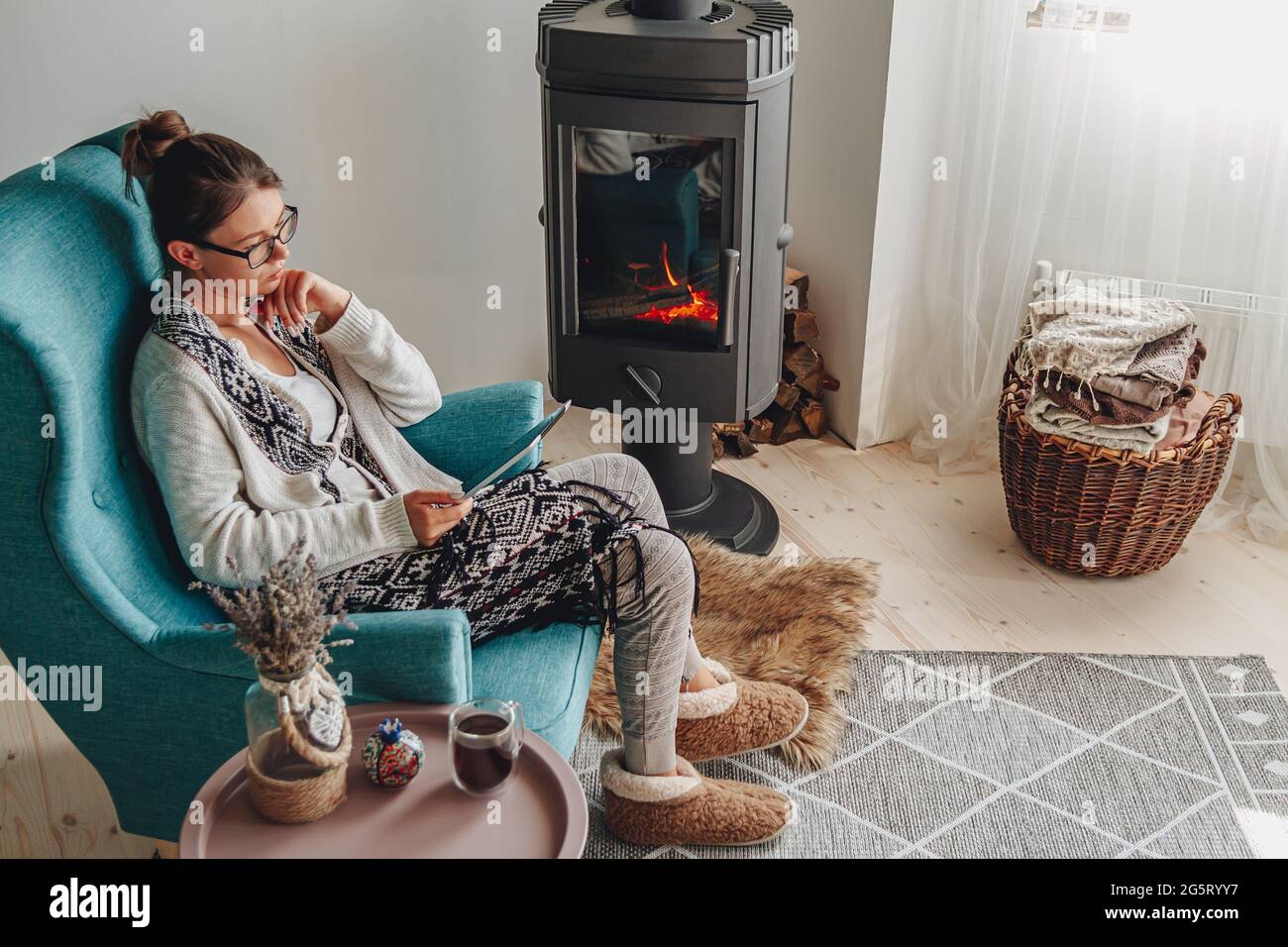 Frau am Kamin, sitzt in einem gemütlichen Sessel, mit einem warmen Stockfoto