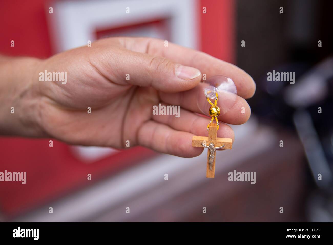 Holzkreuz in der Kirche geweiht. Die Hand hält einen Kreuzanhänger. Kreuz auf den Saugnapf für die Aufhängung im Auto Stockfoto