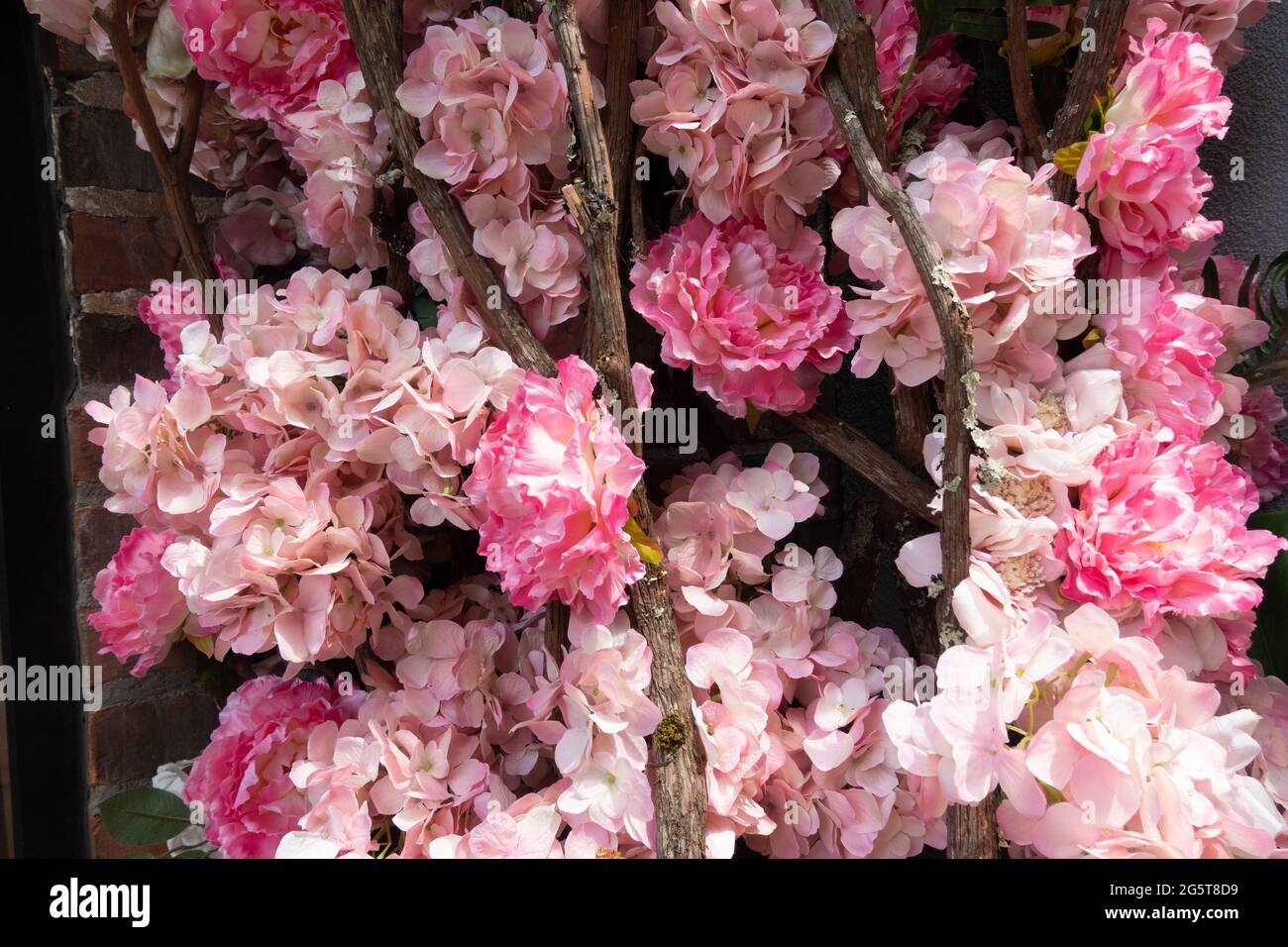 Nahaufnahme eines dekorativen Blumenarrangements mit rosa und hellrosa künstlichen Hortensien und Holzstäben an einer Ziegelwand Stockfoto