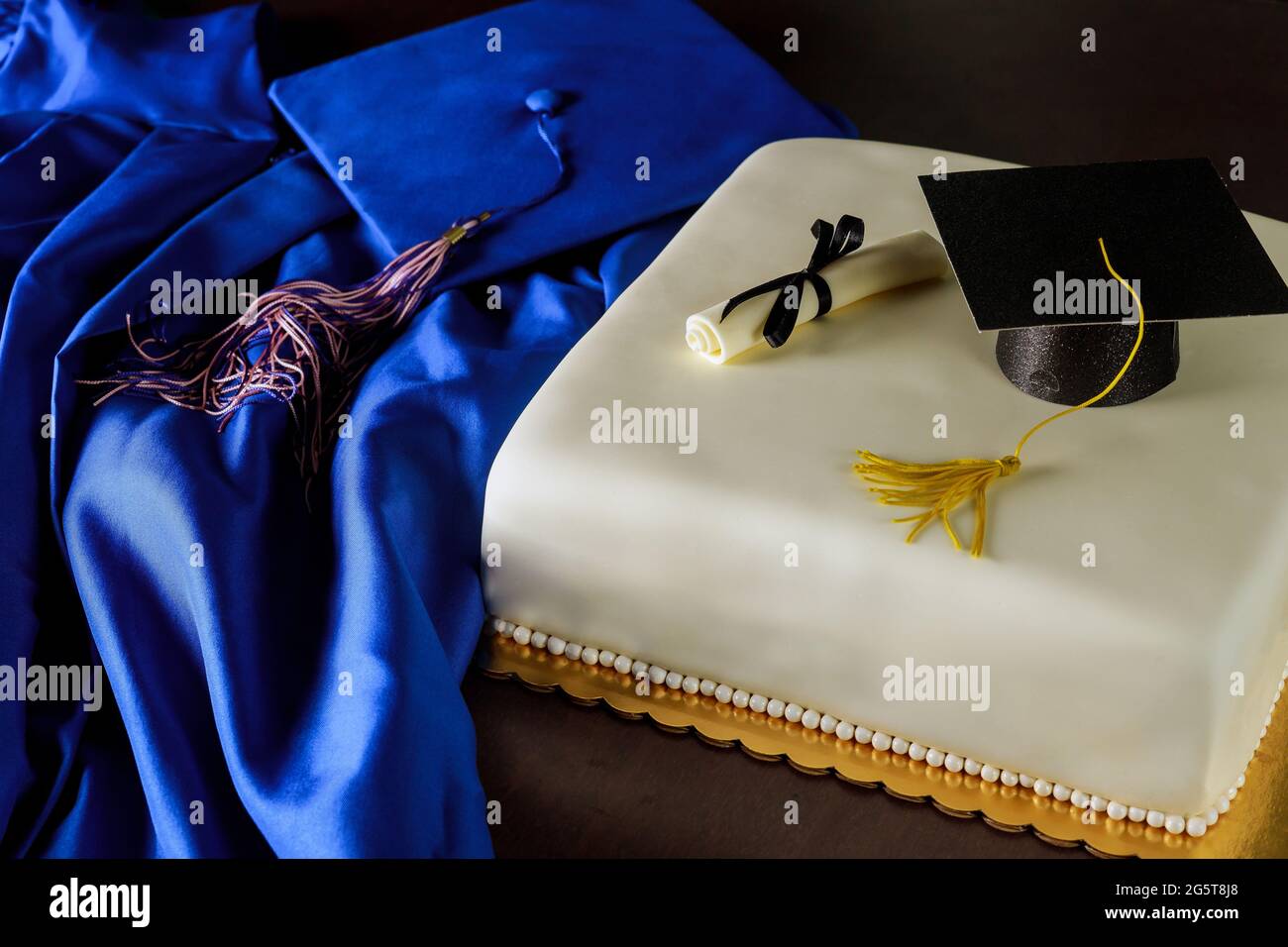 Blaues Abschlusskleid und Mütze mit Kuchen für Schulende. Stockfoto