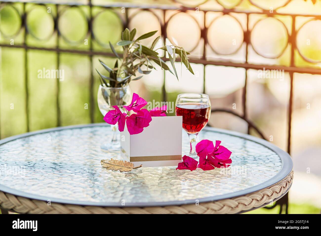 Elegantes Glas Rotwein. Dekorative rosa Blüten von Bougainvillea. Nachbau einer Postkarte oder Einladung. Romantisches Urlaubskonzept. Dekorative grüne lea Stockfoto