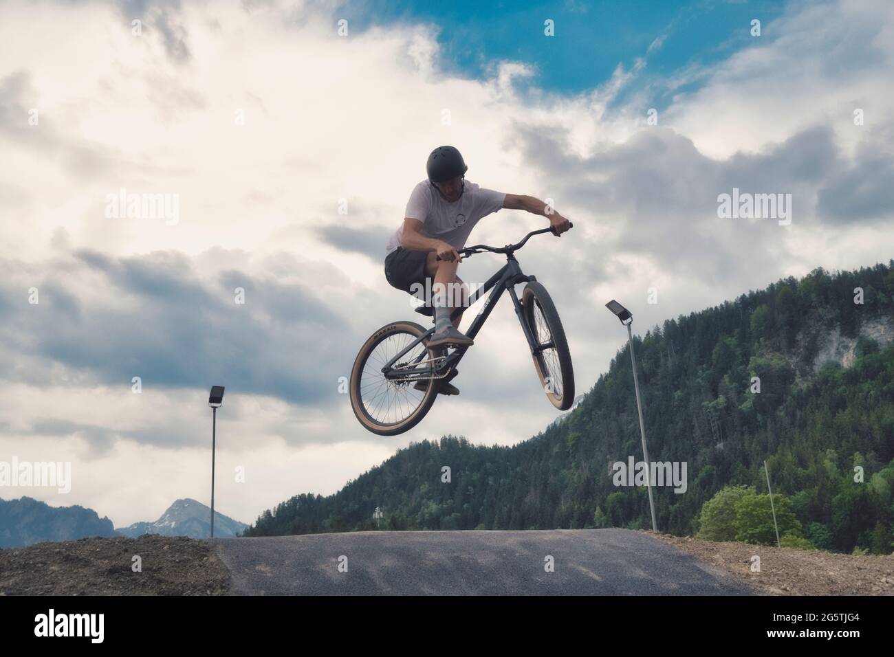 Ein Mann, der durch die Luft fliegt, während er mit dem Fahrrad eine unbefestigte Straße entlang fährt Stockfoto