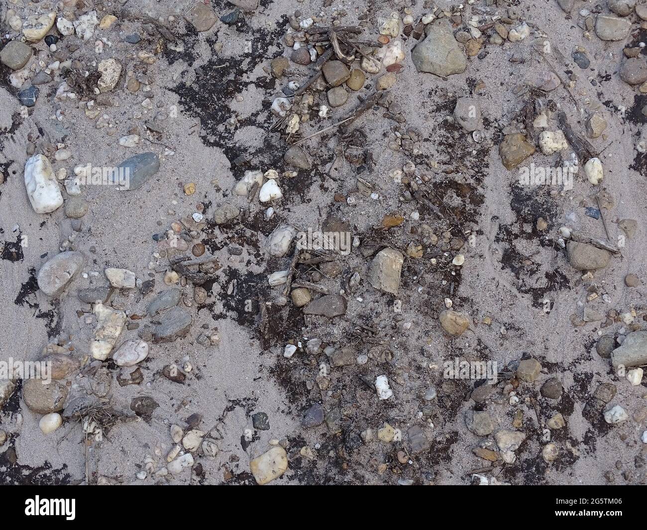 Sand mit Steinen nach einem Regenschauer, grau, weiß, blau und gelb Stockfoto