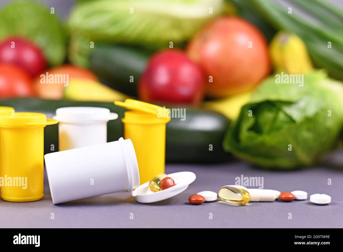 Pillen von Nahrungsergänzungsmitteln verschüttet aus der Flasche vor Obst und Gemüse im Hintergrund Stockfoto