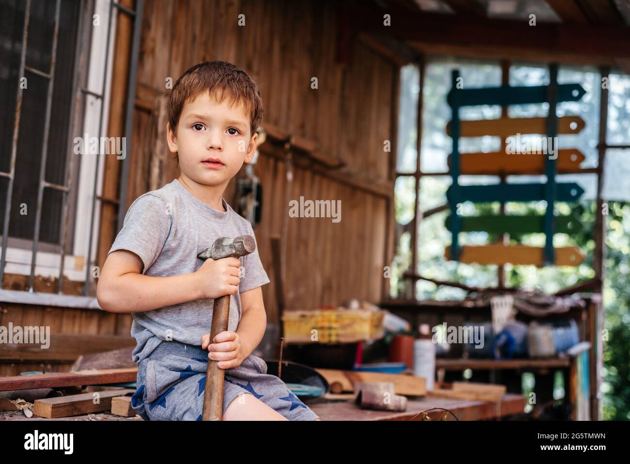 Der kleine Junge hämmert in der Tischlerwerkstatt mit einem Hammer Nägel in ein Holzbrett Stockfoto