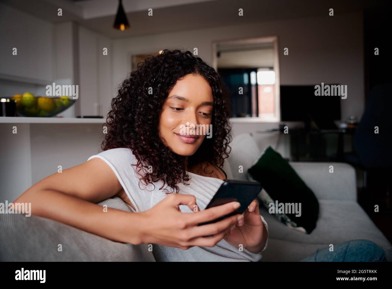 Mischrasse afroamerikanische Frau entspannen auf Couch SMS auf zellulares Gerät Stockfoto