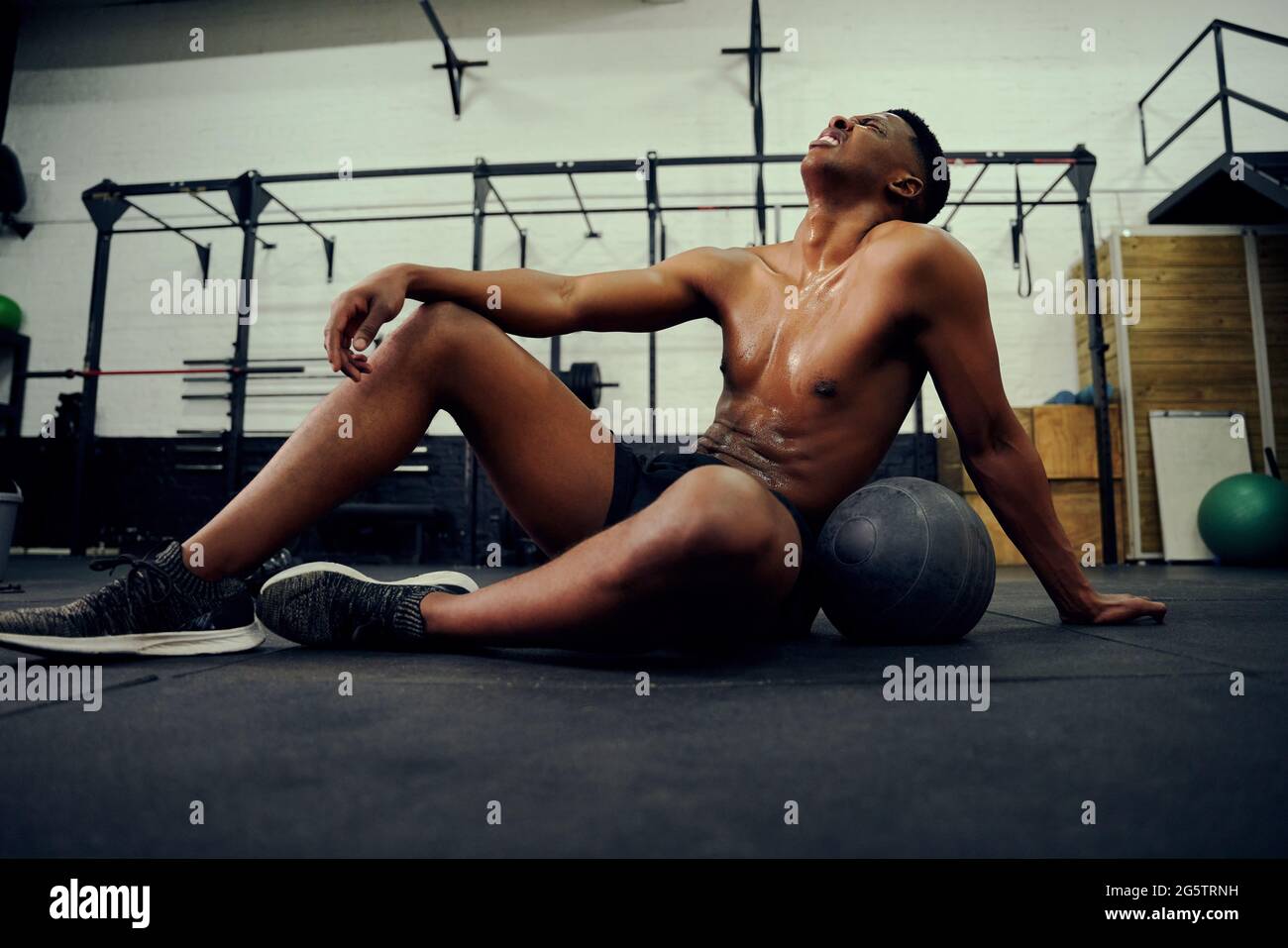 Afroamerikanischer Mann, der sich nach einem intensiven Cross-Training auf dem Hallenboden ausruht. Männlicher Athlet, der nach dem Training erschöpft aussieht. Hohe Qualität Stockfoto