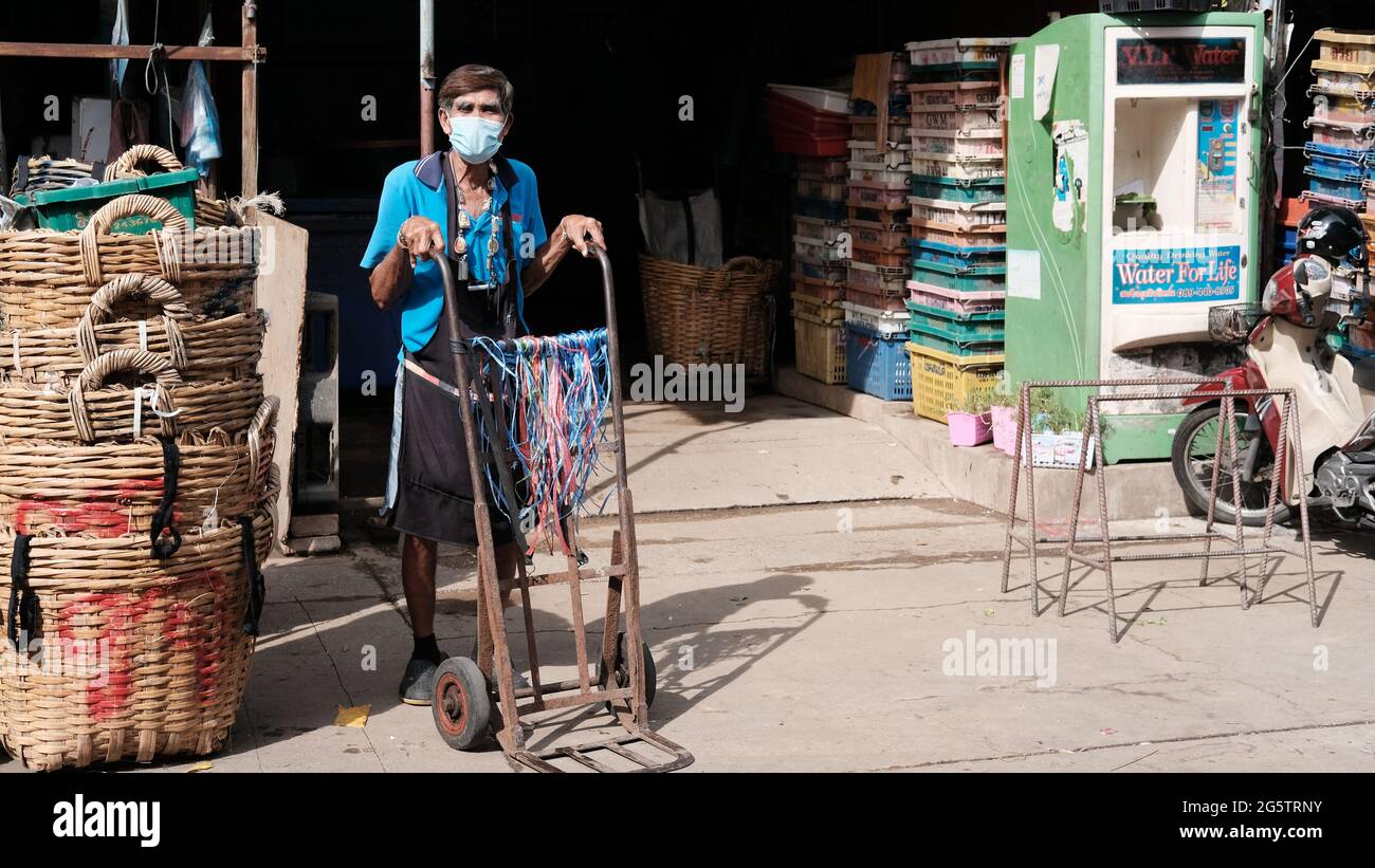 Asian man trägt ein blaues Hemd schwarze Schürze und eine weiße Maske schieben EINEN Hand-LKW arbeiten an urKlong Toey Markt Wet Market Bangkok Thailand Stockfoto