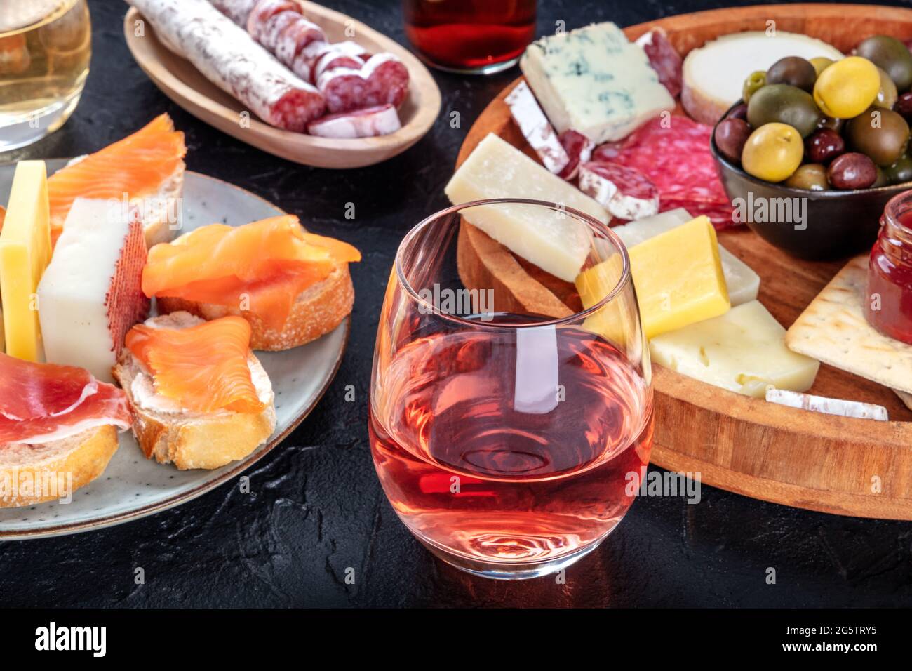 Rosenwein mit Wurstwaren, Käse und Lachs-Sandwiches. Spanische Tapas. Jamon, Fuet, Ziege und Blauschimmelkäse sowie Oliven auf schwarzem Hintergrund Stockfoto