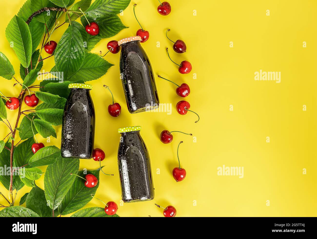 Kalter Kirschsaft in kleinen Glasflaschen mit reifen Beeren und grünen Blättern Stockfoto