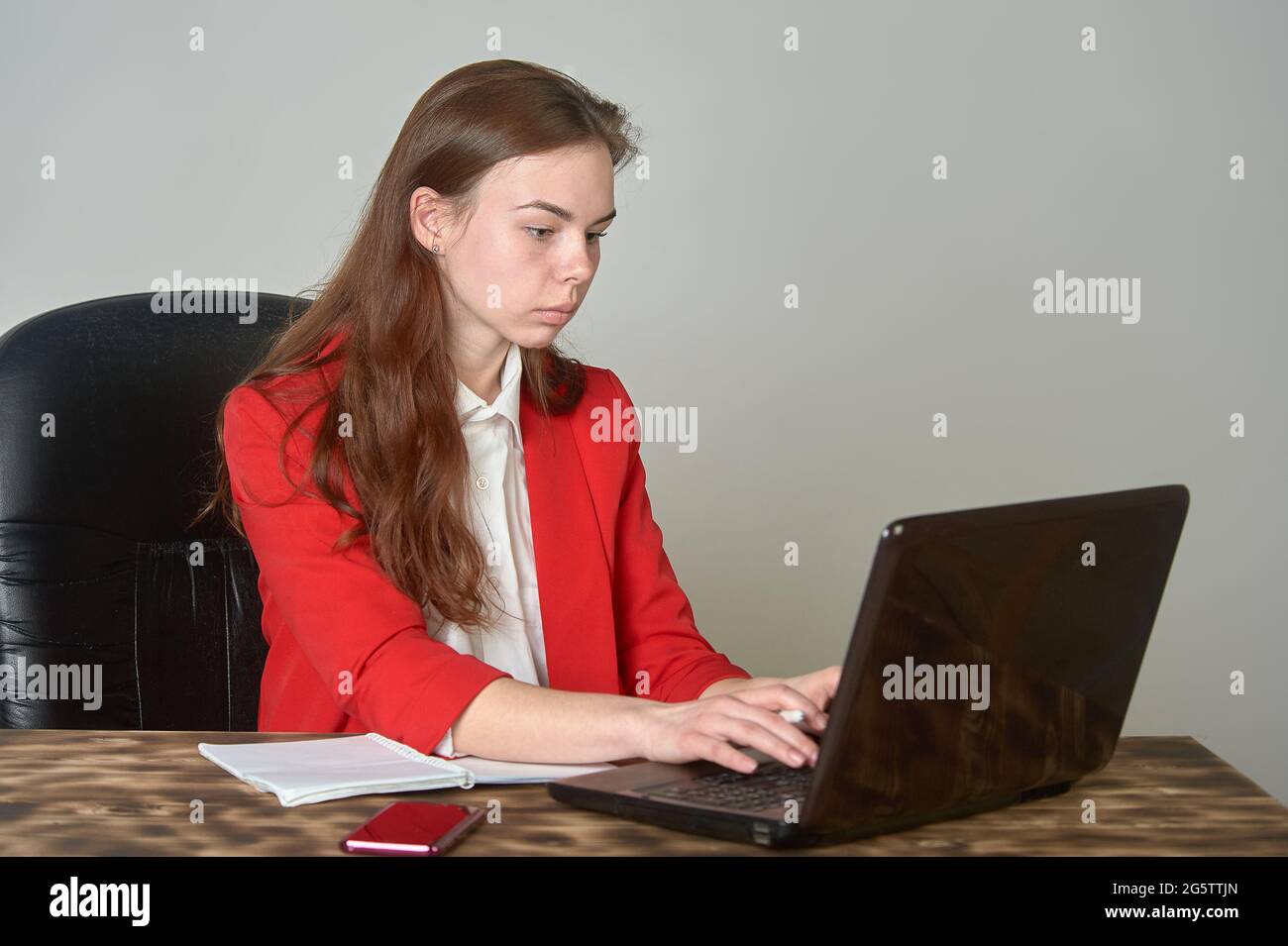 Eine Frau, die an einem Schreibtisch sitzt und mit einem Laptop arbeitet Und Notizblock Stockfoto