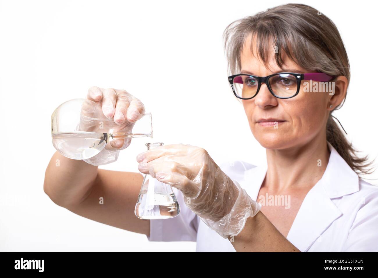 Frau in einem Labormantel, die Flüssigkeit in einen Laborkolben gießt Stockfoto