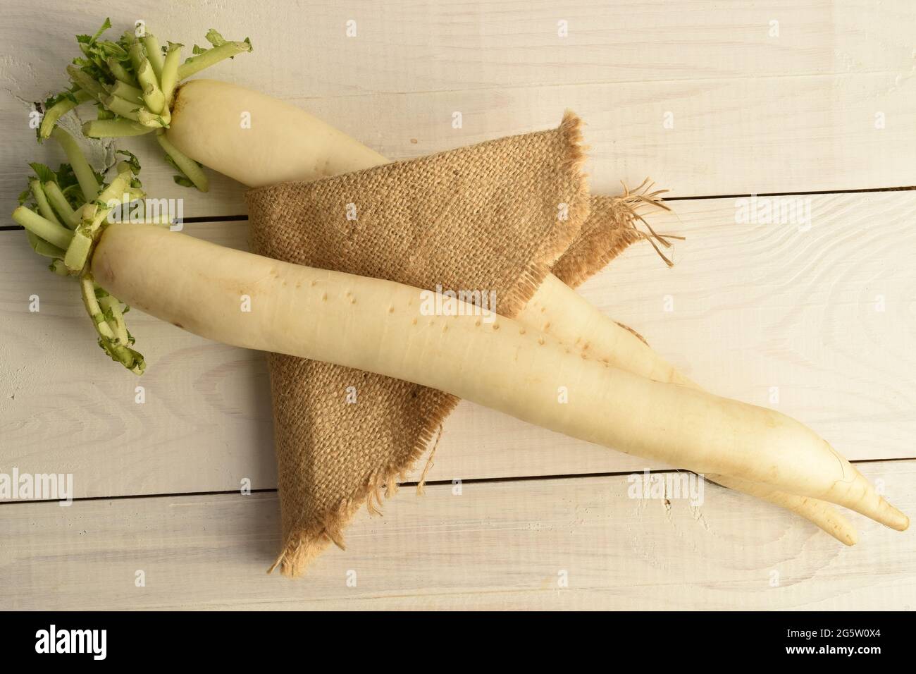 Zwei frische weiße Radieschen mit Jute-Serviette, Nahaufnahme, auf einem weißen Holztisch, Draufsicht. Stockfoto