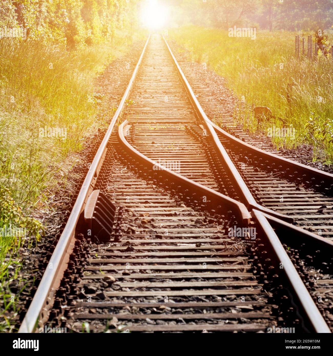 Eisenbahnschienen, mit einem Schalter im Vordergrund, der in die Unendlichkeit führt, mit dem roten Licht der aufgehenden Sonne in der Mitte des Hintergrunds Stockfoto