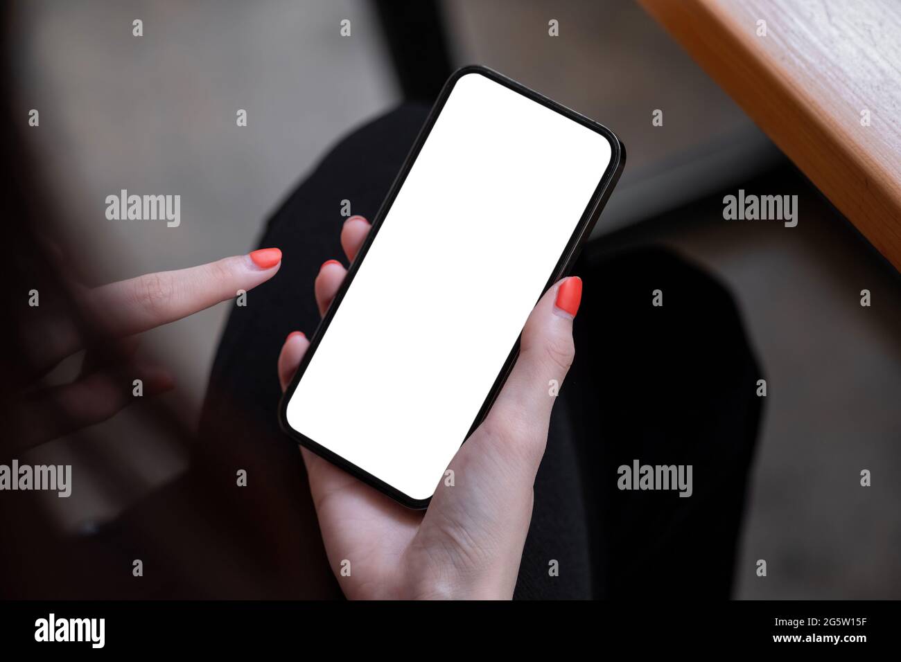 Draufsicht Mockup-Bild einer Frau, die ein schwarzes Mobiltelefon mit leerem weißen Bildschirm hält, während sie im Café sitzt. Stockfoto