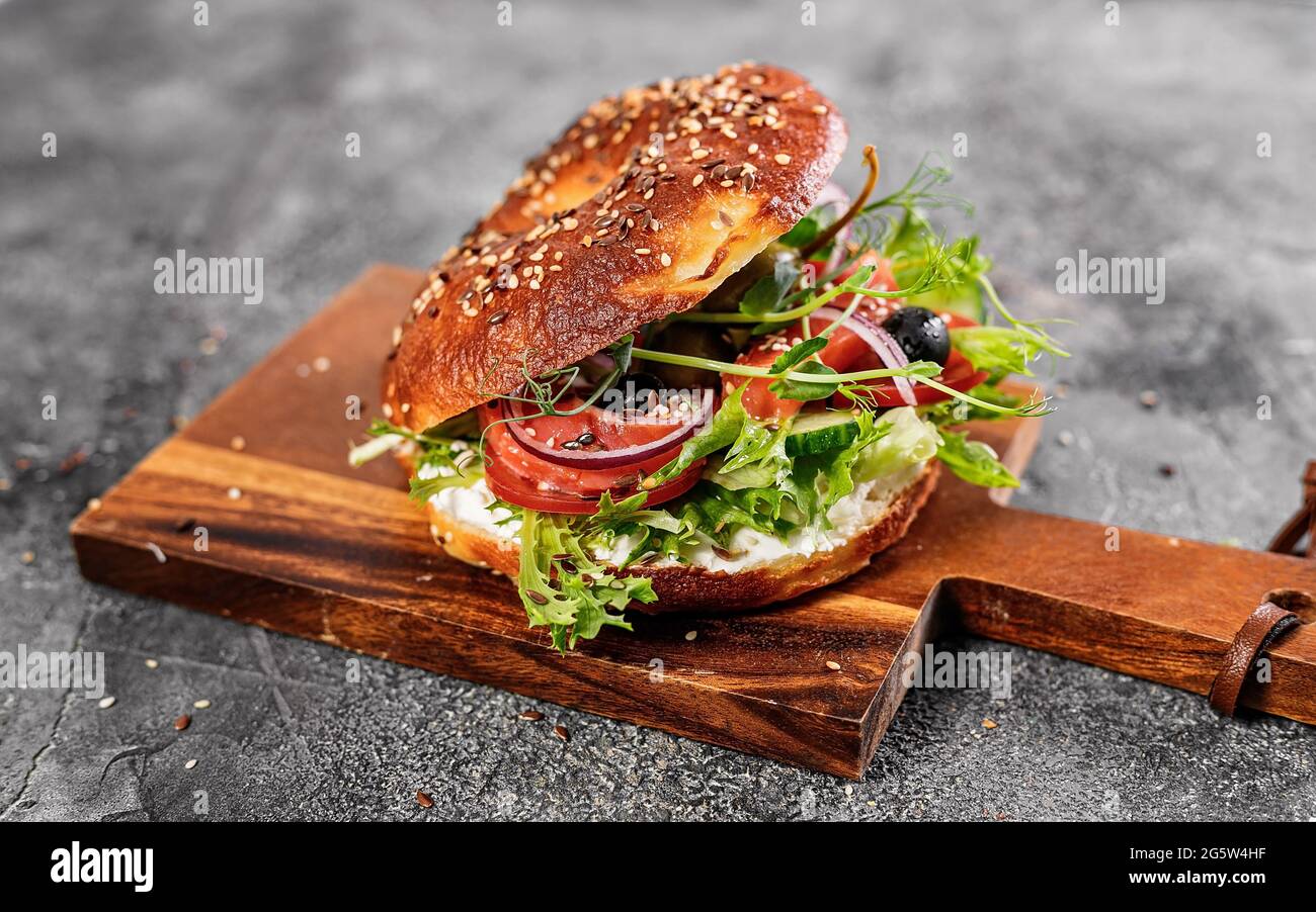 New Yorker Bagel mit Frischkäse, Salat, Gurken, Kräutern, Oliven und gesalzenem rotem Fisch. Hausgemachter Sandwich-Salat auf einem Schneidebrett. Ausgezeichnet lecker Stockfoto