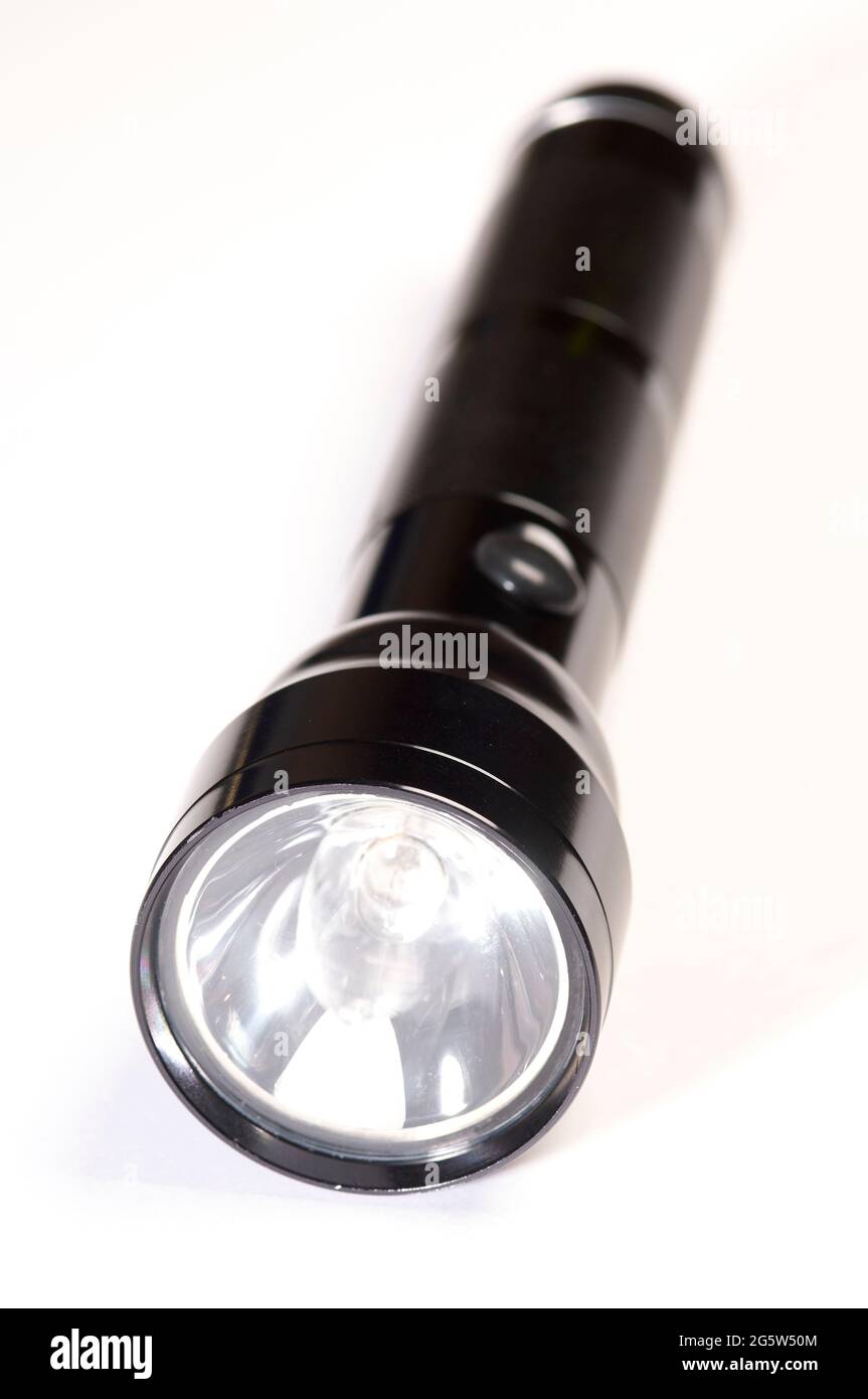 Die kleine schwarze, batteriebetriebene Taschenlampe ist eingeschaltet und befindet sich auf einem weißen Hintergrund, der zur Kamera zeigt Stockfoto