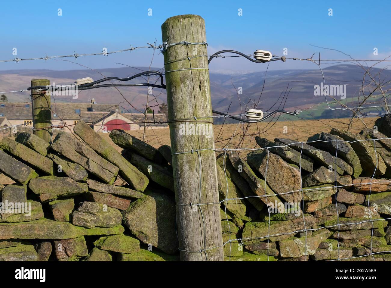 Ein Holzpfosten, der mit Stacheldraht und Kabel an der Spitze einer Trockensteinmauer im Peak District mit offenem Moor in weiter Ferne geführt wird. Stockfoto