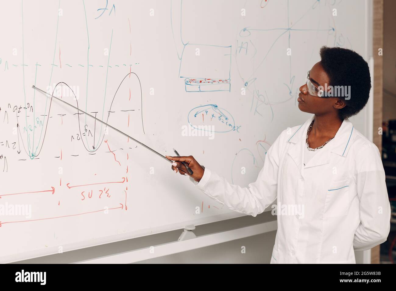 Afroamerikanische schwarze Mathematiklehrerin steht an der weißen Tafel mit Zeiger. Stockfoto