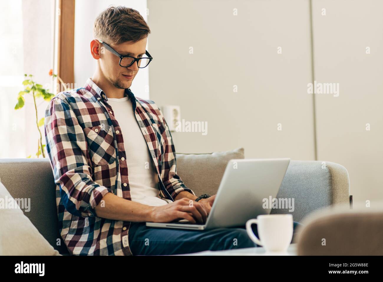 Konzentrierter junger Mann mit Brille, der Laptop benutzt, Text auf der Tastatur tippt, E-Mails oder Nachrichten schreibt, chattet, einkauft, erfolgreicher Freiberufler arbeitet Stockfoto