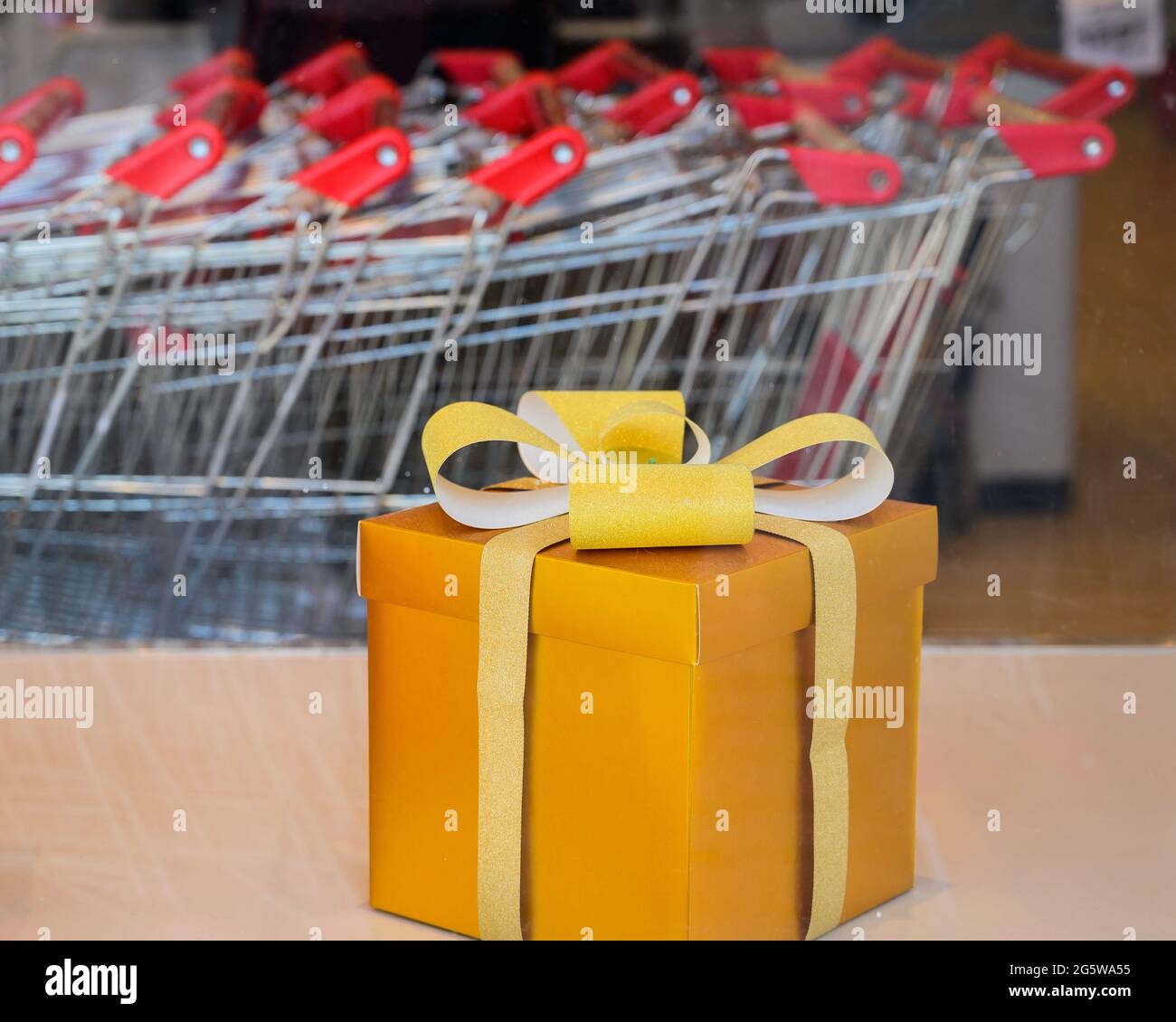 Geschenkbox mit goldenem Schleifband auf dem Hintergrund von Einkaufswagen im Supermarkt Stockfoto