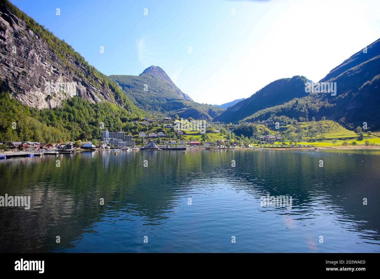 Schöne Aussicht auf Geiranger Stadt vom Wasser aus an einem Sommertag. Spiegelungen der Berge im Fjord. Geiranger, Norwegen. Stockfoto