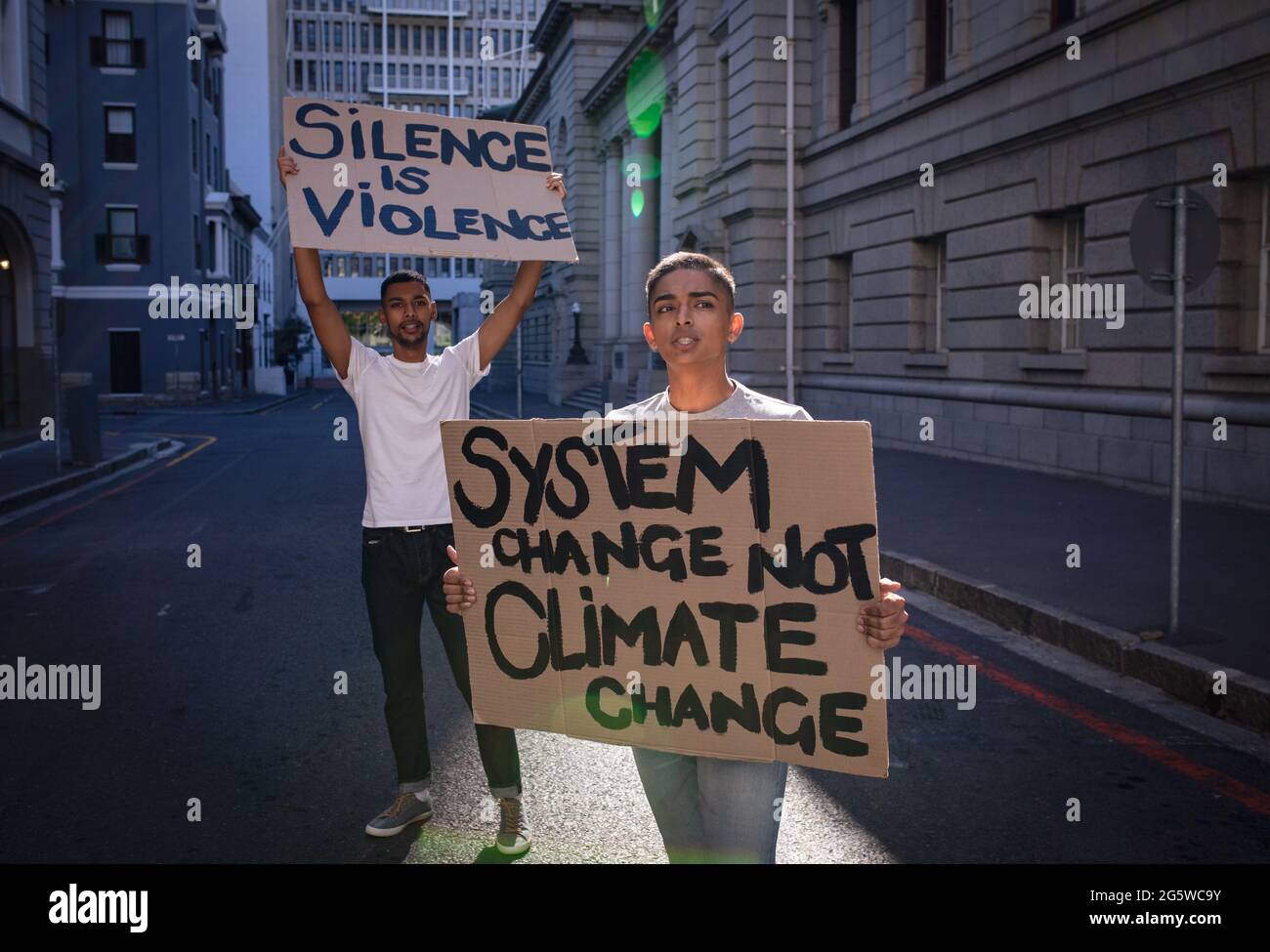 Zwei männliche Freunde mit gemischter Rasse, die handbemalte Protestschilder mit Slogans auf der Stadtstraße tragen Stockfoto
