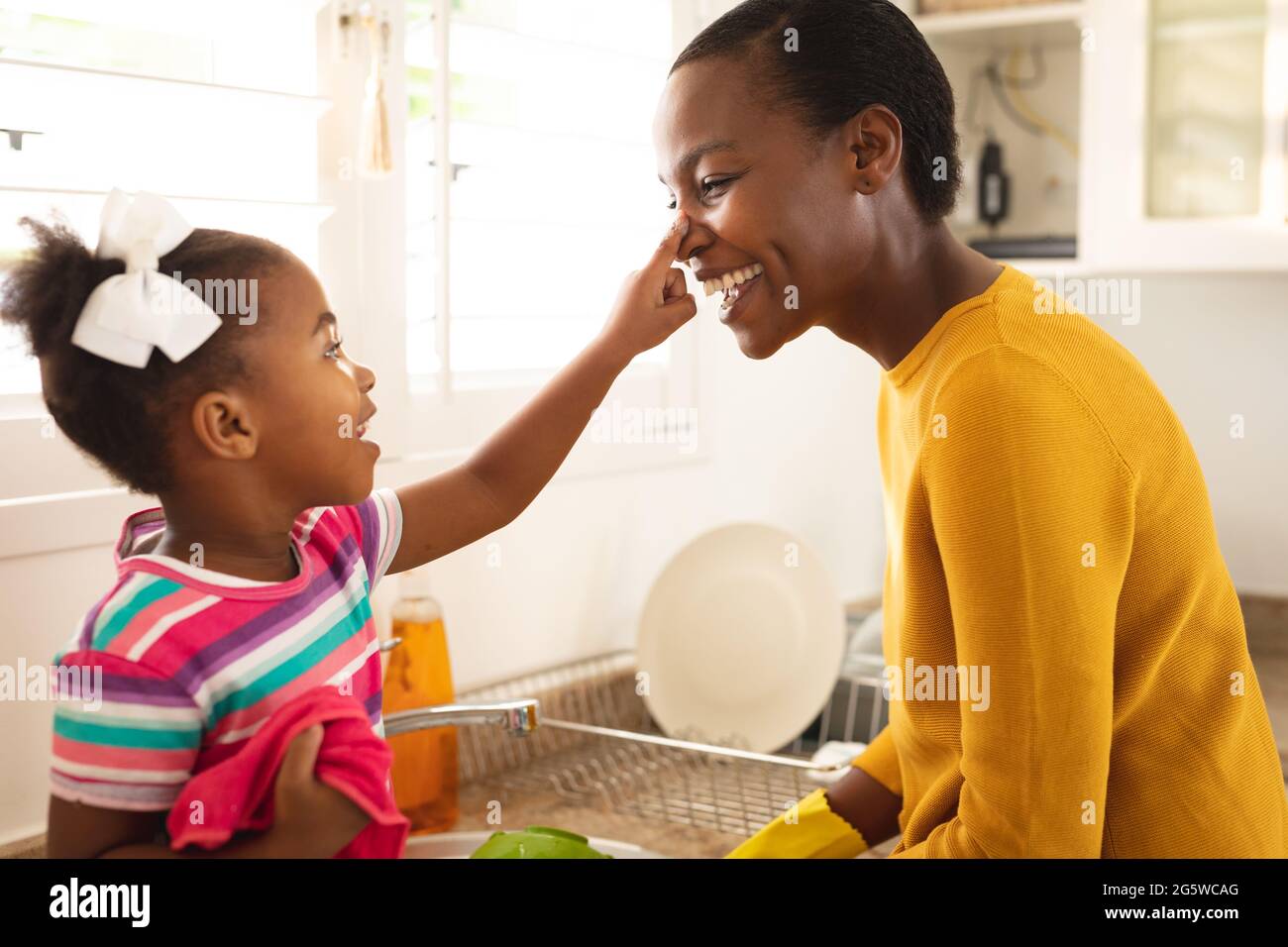 Lächelnde afroamerikanische Mutter und Tochter, die Spaß in der Küche haben, sich zusammen zu waschen Stockfoto