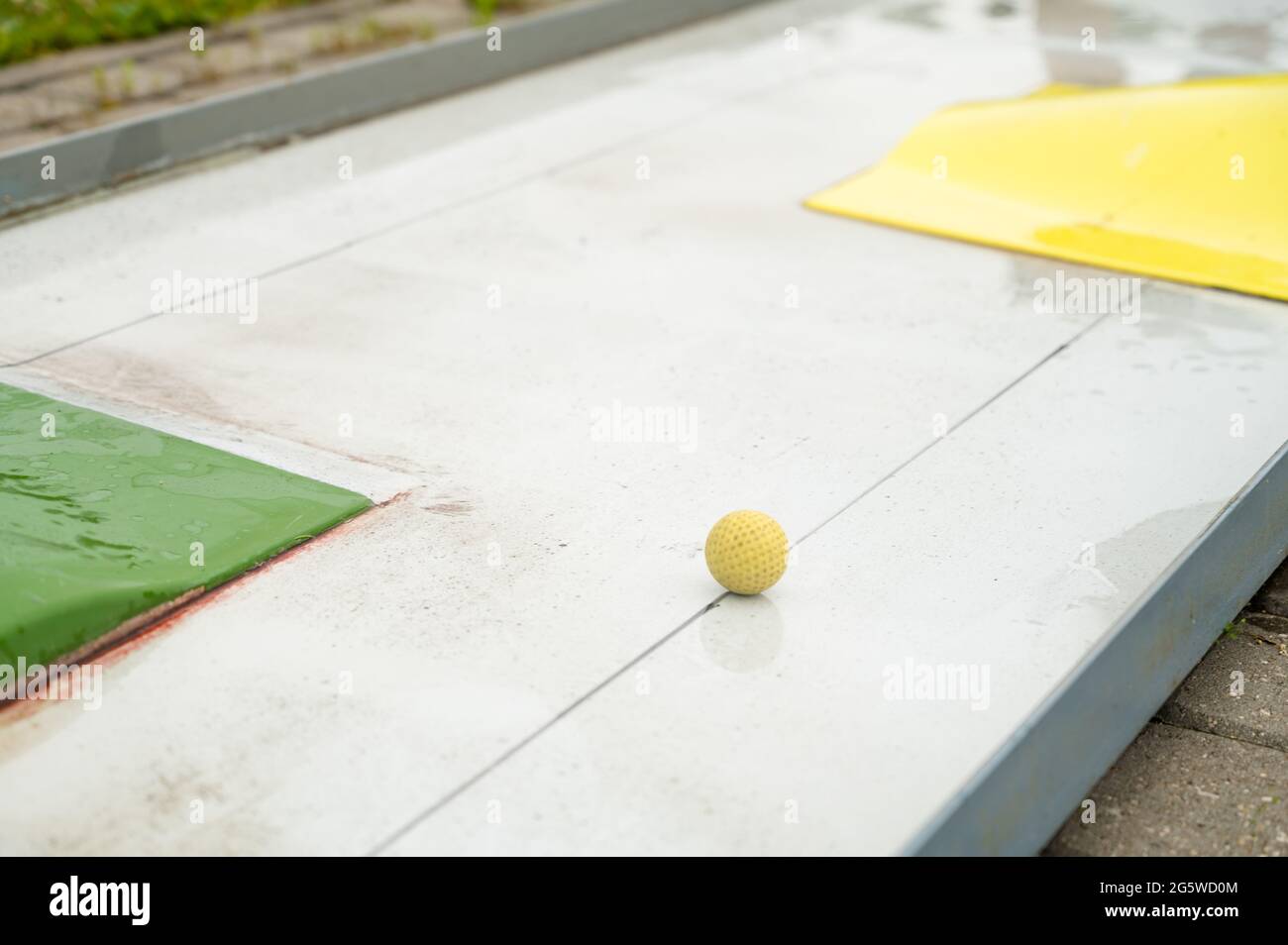 Nahaufnahme des gelben Balls auf dem Minigolfplatz nach Regen. Outdoor-Aktivitäten im Sommer. Stockfoto