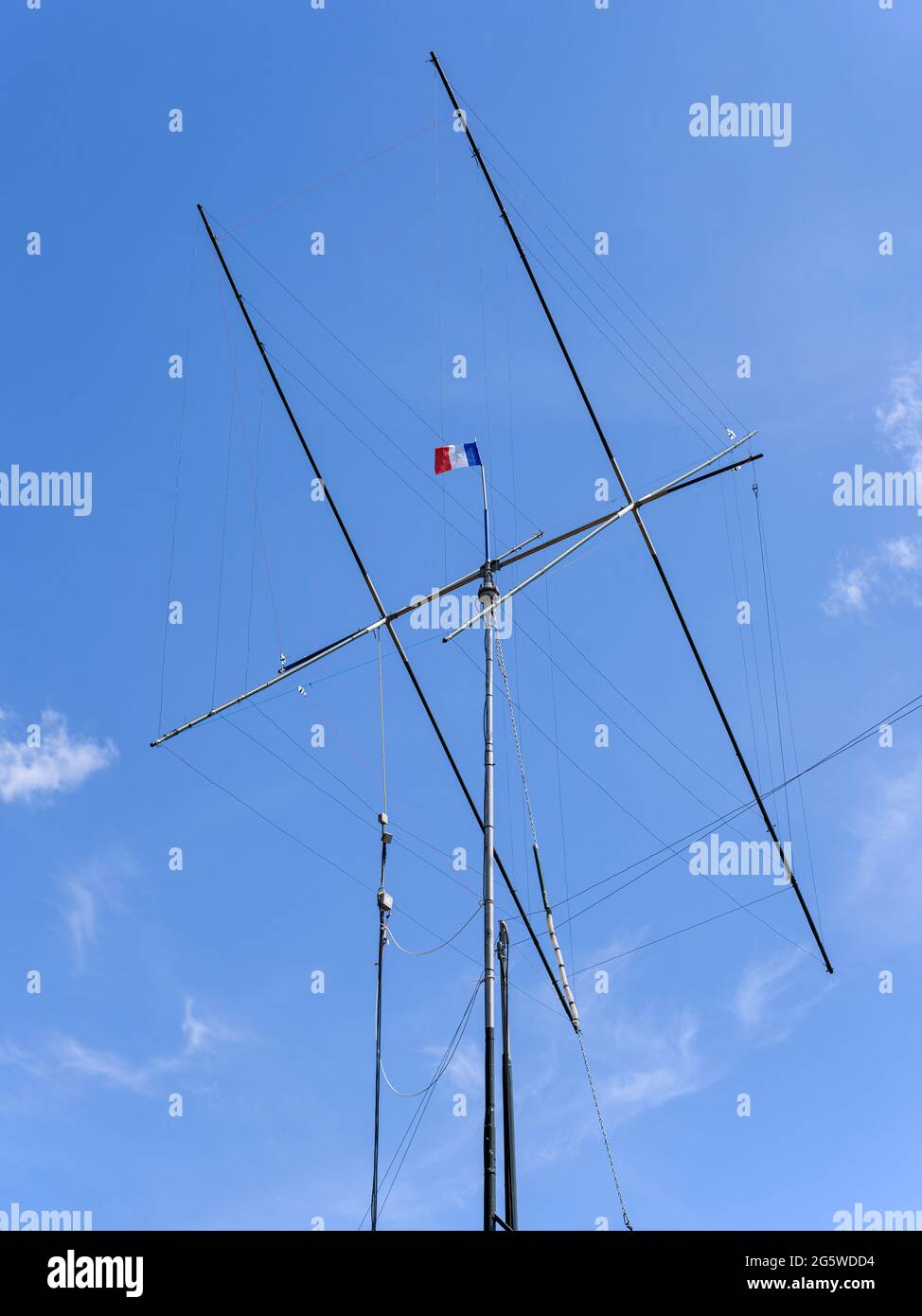 Amateurfunkantenne, die von einer französischen Flagge überragt wird, die im Wind an einem tiefblauen Himmel fliegt. Stockfoto