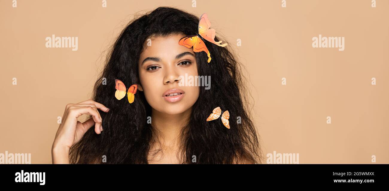 Junge afroamerikanische Frau mit orangen Schmetterlingen auf Haaren isoliert auf beige, Banner Stockfoto