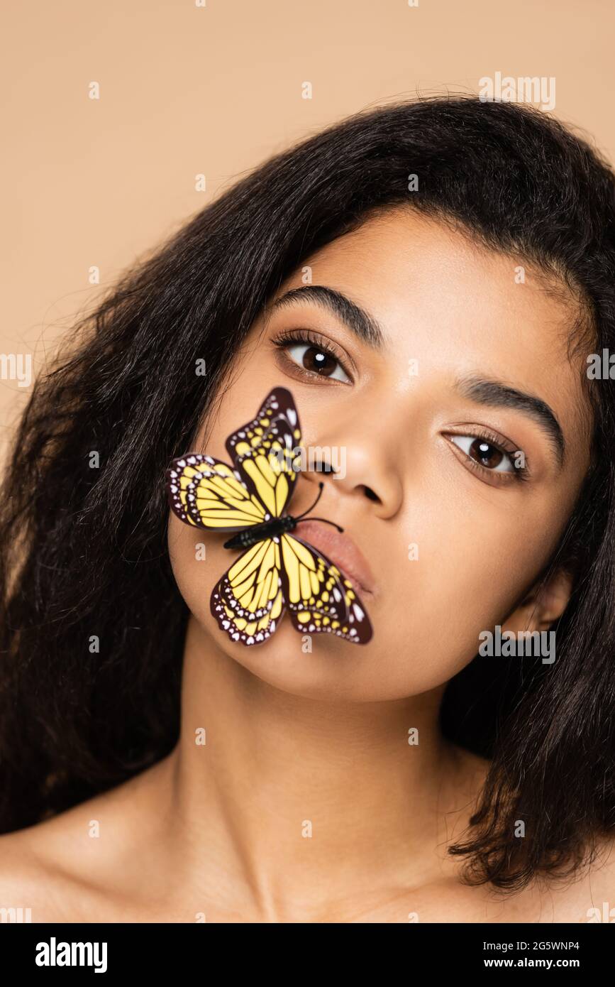 afroamerikanische junge Frau mit Schmetterling auf Lippen isoliert auf Beige Stockfoto
