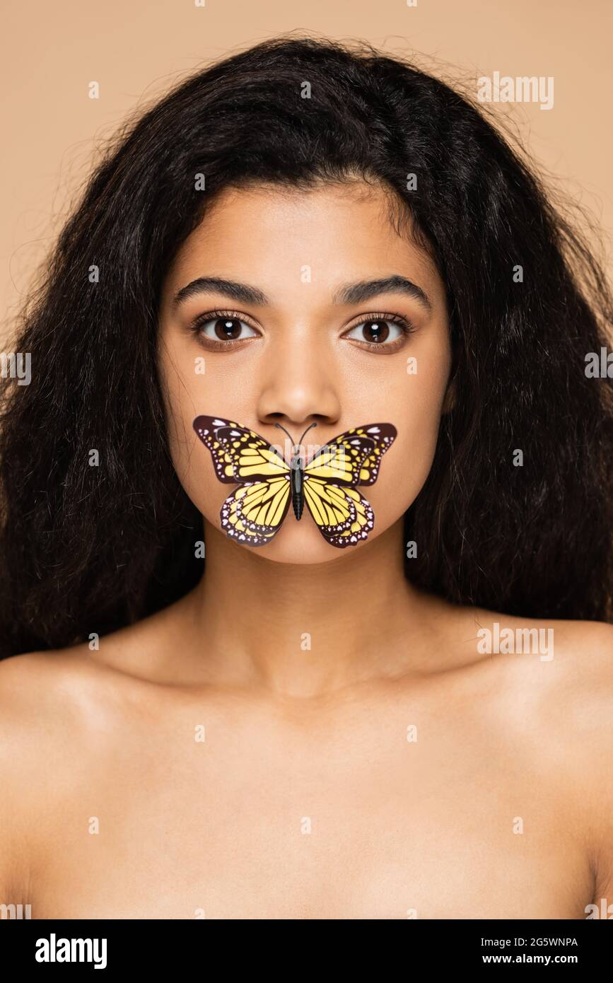 Hübsche afroamerikanische junge Frau mit Schmetterling auf Lippen isoliert auf Beige Stockfoto
