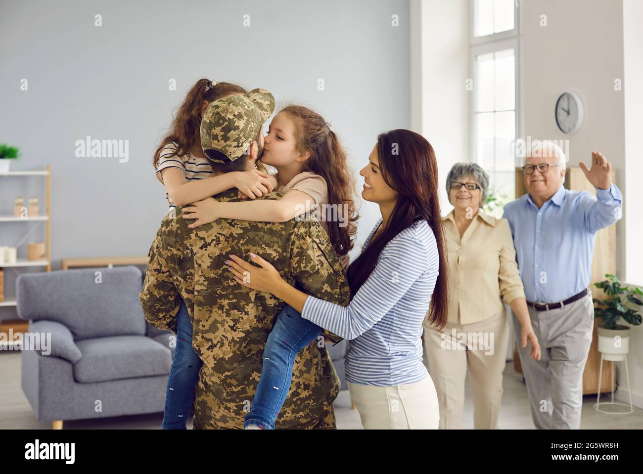 Emotionales Porträt eines unkenntlichen Mannes in Militäruniform, der seine große Familie umarmt. Stockfoto