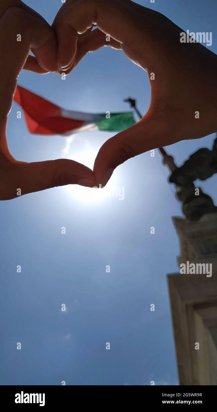 Junge Frau, die die Flagge italiens durch eine Herzform betrachtet, die sie mit ihren Händen gemacht hat Stockfoto