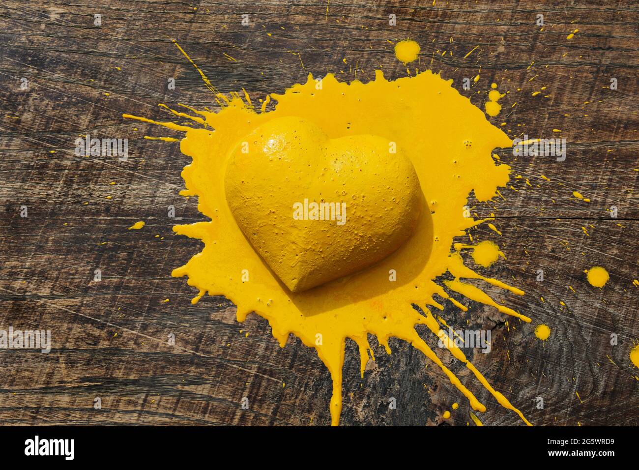 Gelbes Herz. 3 dimensionale Herzform auf Naturholzplatte mit gelber Farbe. Stockfoto